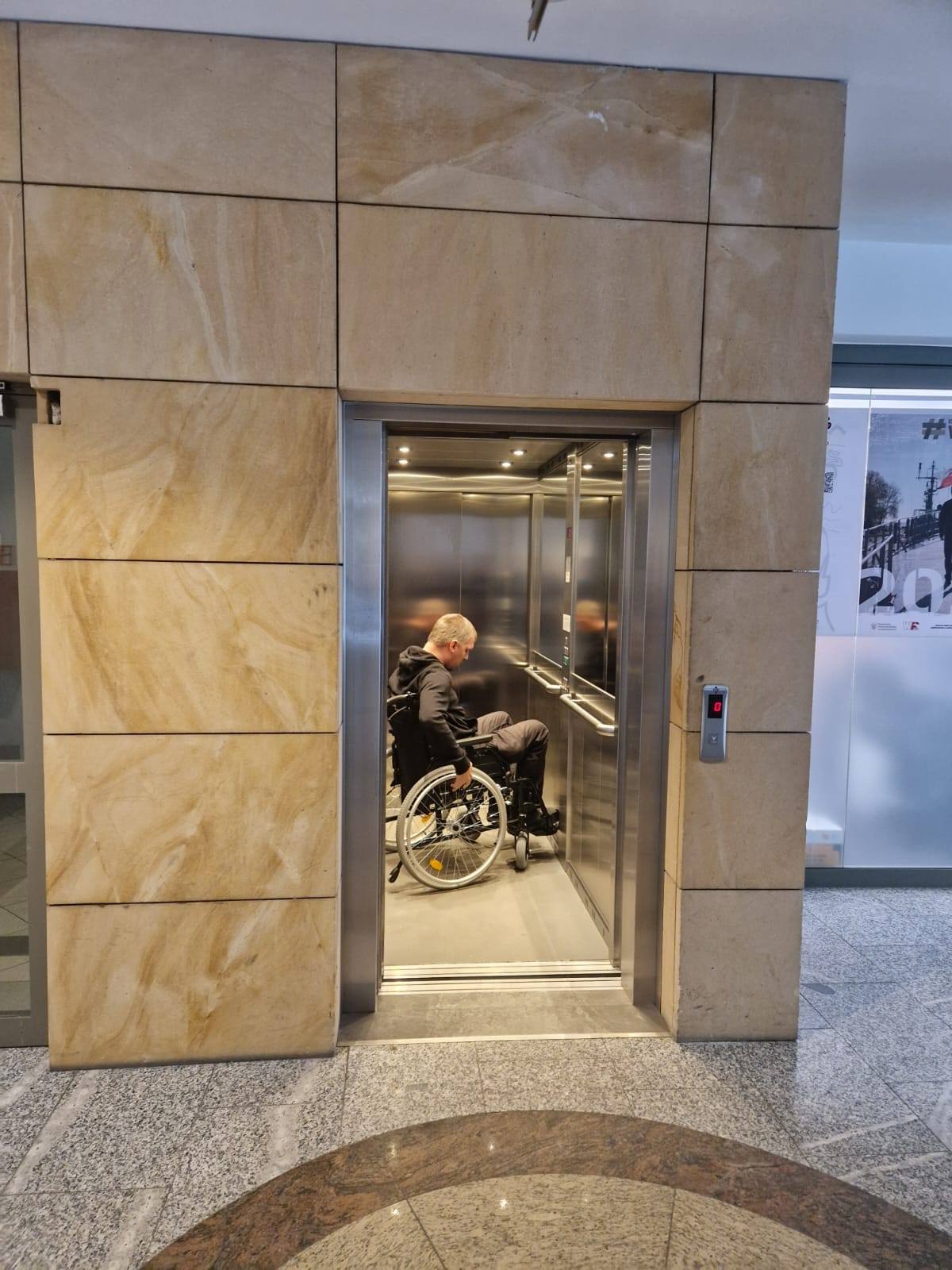 Osoba podczas wjeżdżania wózkiem do windy.